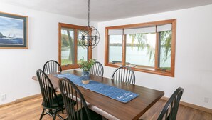 A dining area with a wooden table, six chairs, a vase with a plant, and a blue placemat.