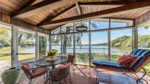 A covered patio with a table and chairs, a cushioned seating area, and a view of a lake.
