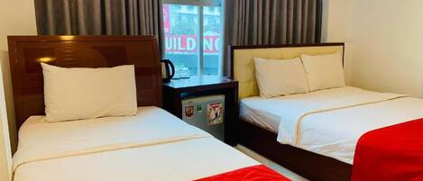 Una habitación de hotel con dos camas, una mesita de noche y un ventanal con cortinas.