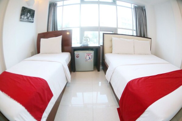 A hotel room with two beds, a small table with a refrigerator, and a window with curtains. - Nu hotel (Ho Chi Minh City)