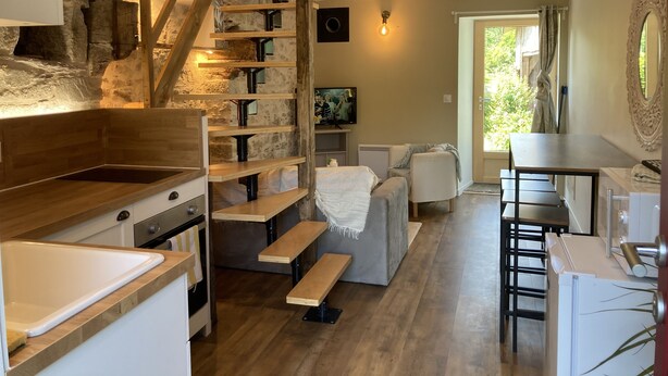 A modern kitchen with a wooden staircase, a dining area with a table and chairs, and a cozy living space with a sofa and a TV.