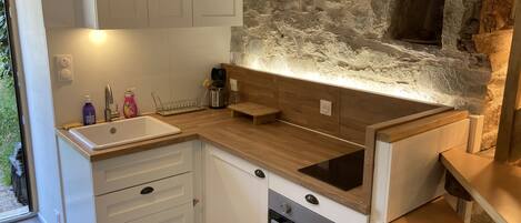 A compact kitchen with white cabinets, a wooden countertop, a built-in oven, and a stone wall.