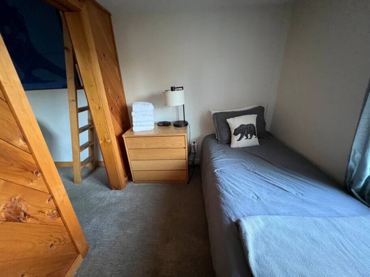 Une chambre avec un lit en mezzanine, une table de chevet en bois avec une lampe et un lit simple avec un oreiller.