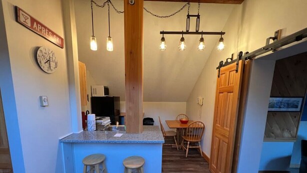 Een kleine keuken met een centraal eiland, houten stoelen en hanglampen.