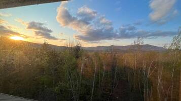 Vista desde una ventana sobre un paisaje boscoso con montañas al fondo durante el atardecer.