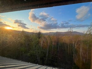 Aussicht vom Fenster auf eine bewaldete Landschaft mit Bergen in der Ferne bei Sonnenuntergang.