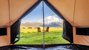 Ein Zelt mit freiem Blick auf eine Wiese und Berge im Hintergrund.