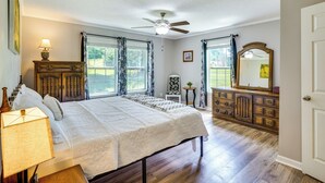 Ein Schlafzimmer mit Bett, Schminktisch, Deckenventilator und einem Fenster mit Vorhängen.