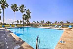 A swimming pool with clear blue water, surrounded by palm trees and lounge chairs.