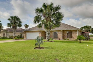 A residential house with a well-maintained lawn, palm trees, and a garage.