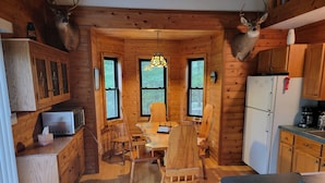L’intérieur d’un chalet avec des murs en bois, une table à manger, des chaises, un réfrigérateur et des bois de cerf fixés aux murs.
