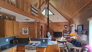 L’intérieur d’une cabane est composé de murs en bois, d’une cuisine avec un poêle, d’un espace de vie avec un canapé et d’un téléviseur.