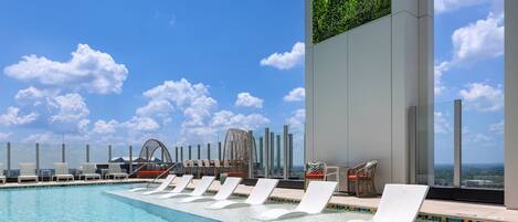 A rooftop pool with white lounge chairs and a view of the ocean.