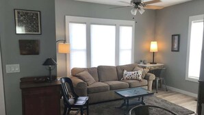 A living room with a sofa, coffee table, and chairs. There is a desk with a lamp, a ceiling fan, and a window with blinds. - Blue Maple Cottage in Downtown Traverse City (Traverse City)