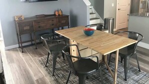 A dining area with a wooden table, black chairs, a bowl, a television, a staircase, and a kitchen area. - Blue Maple Cottage in Downtown Traverse City (Traverse City)
