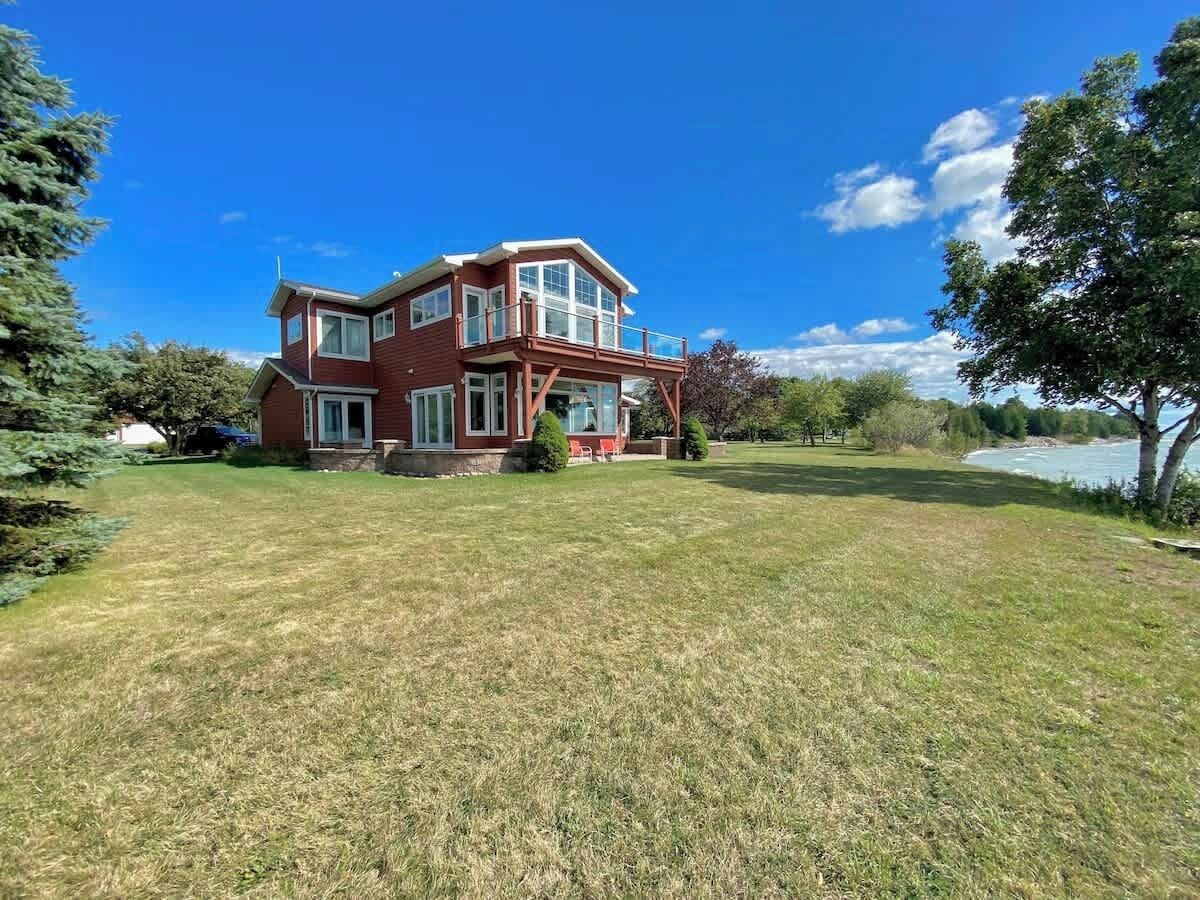 Una casa de dos pisos con un amplio jardín delantero, un balcón y vista a un lago.