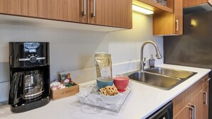 Et moderne køkken med træskabe, en stålvask, en kaffemaskine og en bakke med mad.
