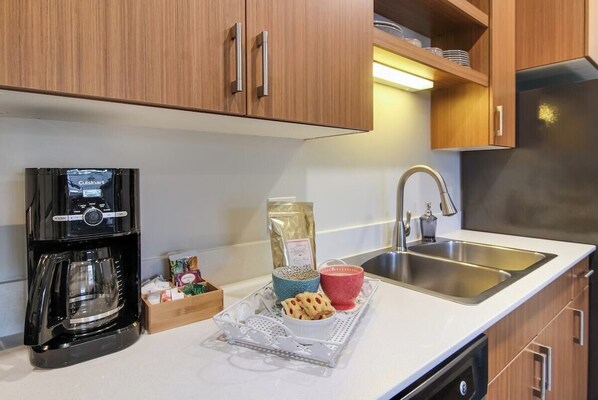 A modern kitchen with wooden cabinets, a stainless steel sink, a coffee maker, and a tray with food items. - Trailside Condo in Traverse City (Traverse City)