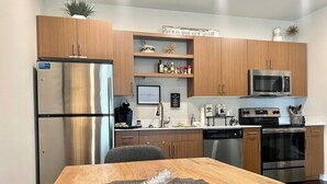 A modern kitchen with stainless steel appliances, wooden cabinets, and a dining area with a placemat. - Stylish Traverse City Condo with Balcony (Traverse City)