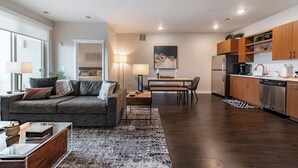 A modern living room with a gray sofa, a coffee table, and a dining area with a table and chairs. The kitchen features wooden cabinets and stainless steel appliances. - Stylish Traverse City Condo with Balcony (Traverse City)