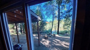 Uitzicht door een raam op een overdekt buitengebied met een barbecue, houten constructies en bomen.