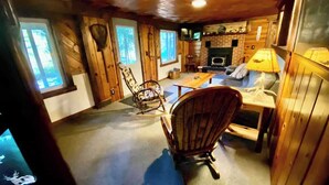 Een gezellig houten interieur met een open haard, schommelstoelen en een eettafel.