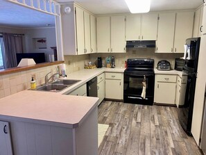 A compact kitchen with light-colored cabinets, a black stove, and a sink.