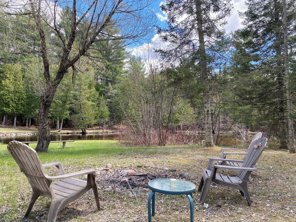 Ein Campingplatz mit zwei Adirondack-Stühlen und einem kleinen runden Tisch mit einer Kerze.