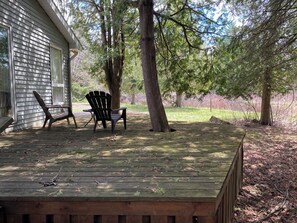 Una terrassa de fusta amb dues cadires Adirondack, una casa i arbres al voltant.