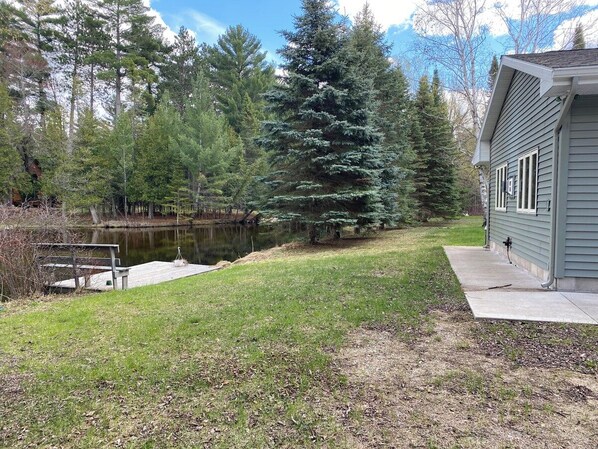 A house with a dock extending into a pond, surrounded by trees. - Secluded Riverfront Home in Grayling (Grayling)