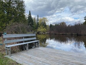 A wooden dock extending into a calm body of water, surrounded by trees and a cloudy sky. - Secluded Riverfront Home in Grayling (Grayling)