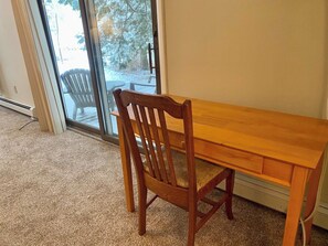 A wooden dining table with a chair in a room with carpeted flooring and a view through a glass door.