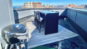 Eine Dachterrasse mit Grill, Tisch und Stühlen.