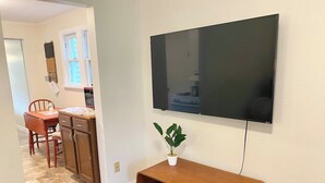 A living room with a flat-screen TV mounted on the wall, a wooden entertainment unit, and a potted plant. - Convenient 2 Bedroom Home in Traverse City (Traverse City)