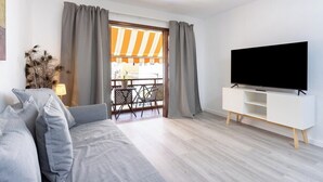 A modern living room with a grey sofa, a flat-screen TV on a white stand, and a balcony with striped awnings.