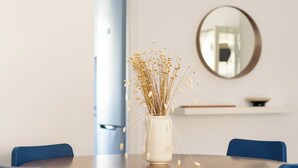 Et rundt spisebord med en hvid vase med tørrede blomster i midten, omgivet af blå stole.