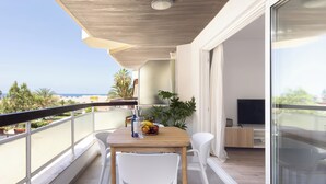 En balkon med et træbord, hvide stole, en skål med frugt og et fjernsyn på et træstel.