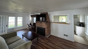 A living room with a fireplace, wooden flooring, and a dining area with a table and chairs.