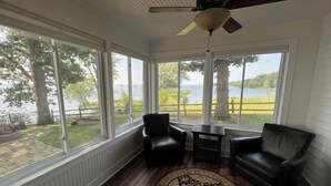 A sunroom with large windows, a ceiling fan, and a view of a lake.