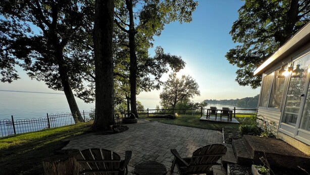 An outdoor patio with stone flooring, wooden chairs, and a view of a lake.