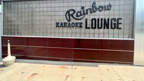 Fachada de un edificio con un gran letrero que dice 'Rainbow Karaoke Lounge'.