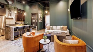 Une cuisine moderne avec un coin bar, un salon doté d’un canapé et de fauteuils, et un téléviseur à écran plat fixé au mur.
