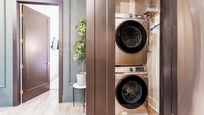 Un espace buanderie compact comprenant un lave-linge et un sèche-linge Samsung, une petite plante posée sur une table d’appoint et une porte donnant sur une autre pièce.