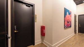 Un couloir doté d’un plancher en bois, de portes noires, d’un extincteur et d’une affiche accrochée au mur.