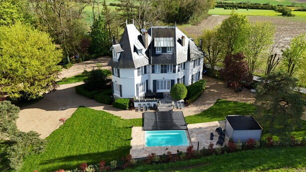 Une grande maison à deux étages, dotée d’une piscine, entourée de pelouses et d’arbres bien entretenus.