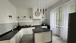 Une cuisine moderne avec des armoires blanches, un comptoir noir et un îlot central. On y trouve des luminaires suspendus, une horloge au mur et une fenêtre avec des rideaux.