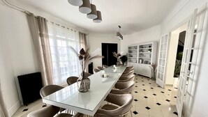Un espace repas avec une longue table, plusieurs chaises et des luminaires suspendus.