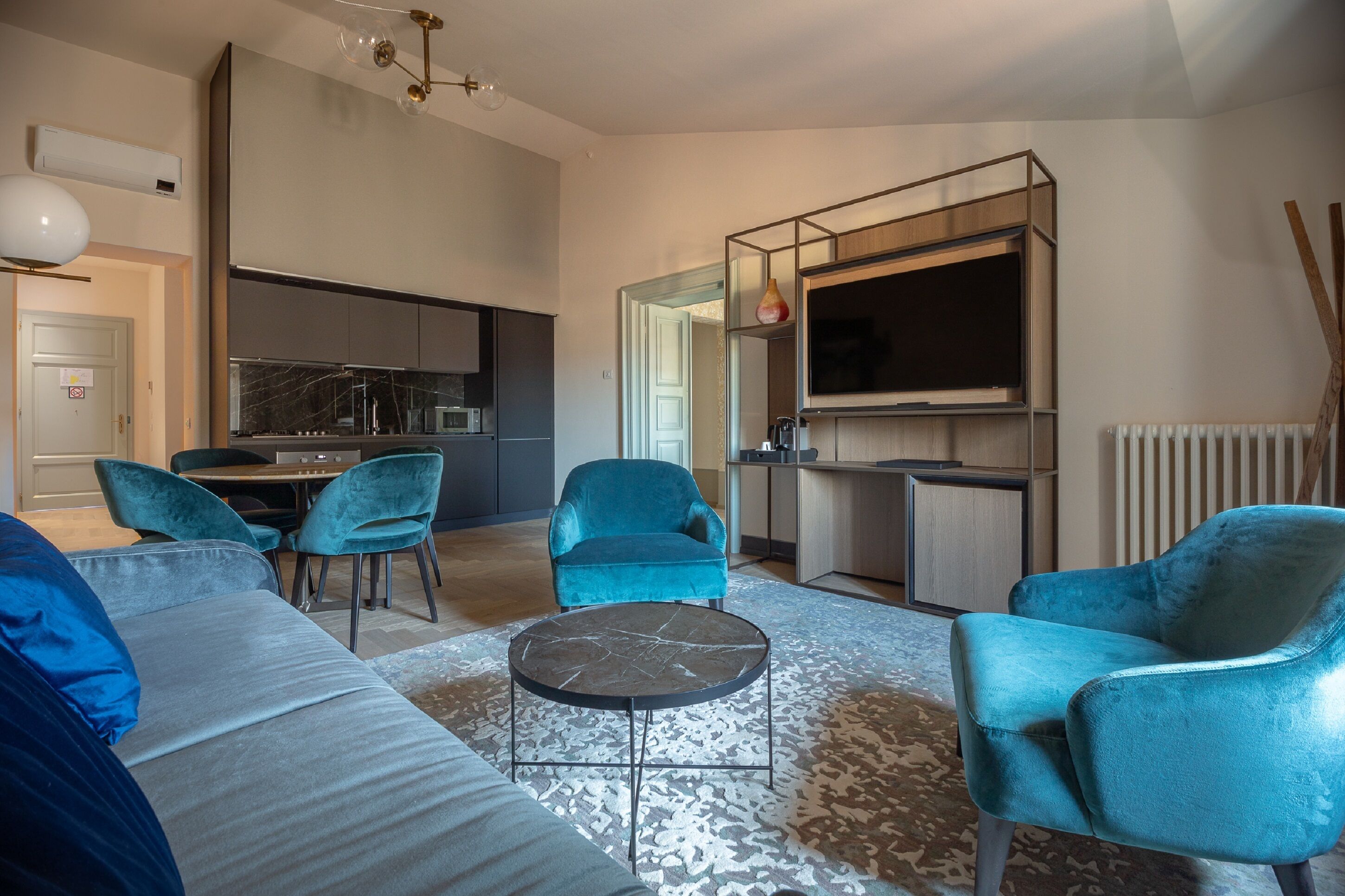 A modern living room with a sofa, two blue armchairs, a coffee table, and a TV mounted on a wooden wall.