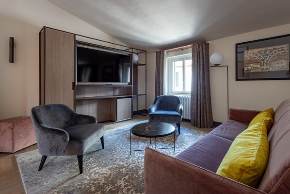 A modern living room with a sofa, two armchairs, a coffee table, and a TV on a wall unit. - Grand Universe La Residenza (Lucca)