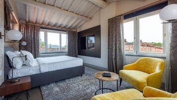 A bedroom with a bed, a TV, a small round table, and two yellow chairs.